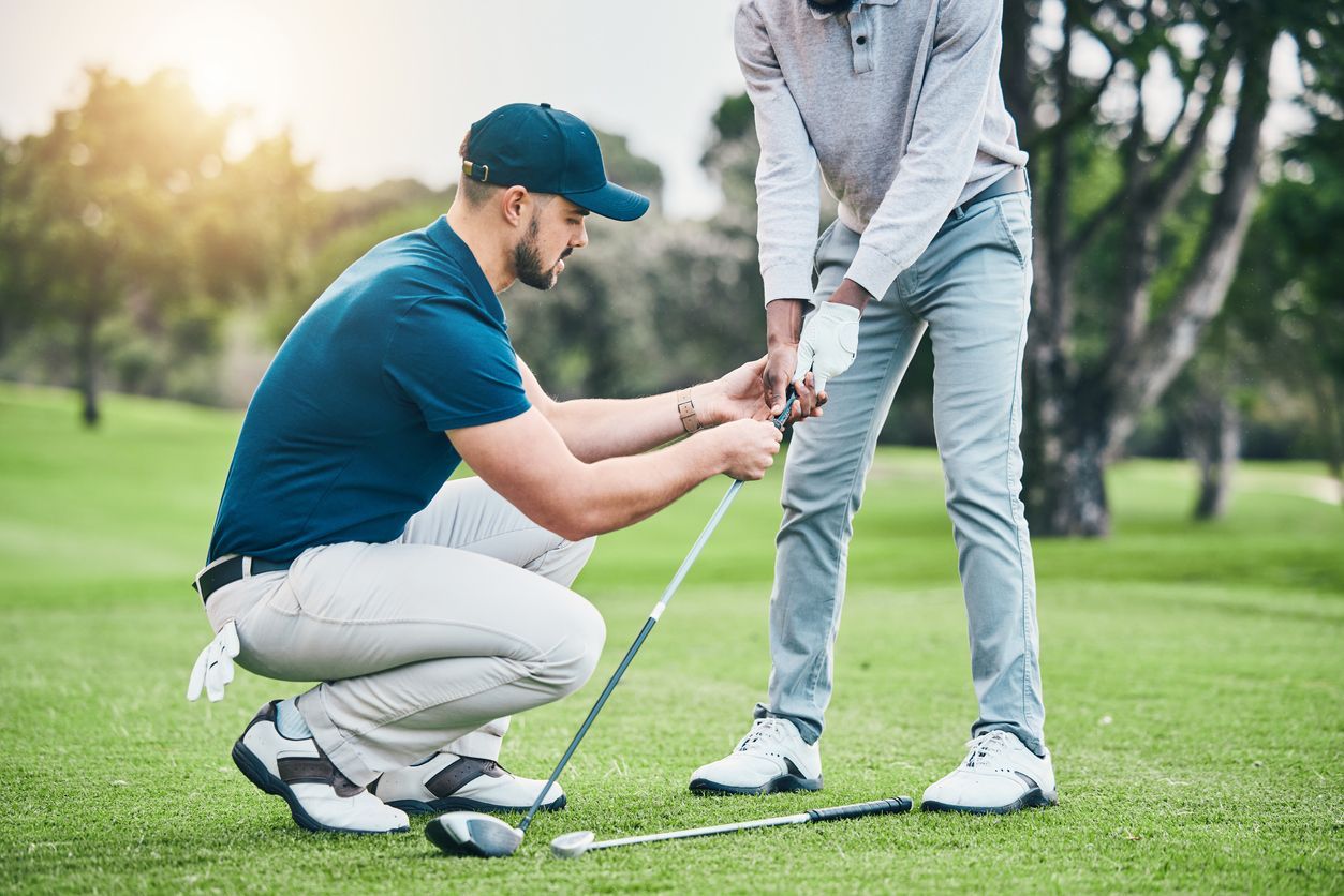 A golf instructor helps a golfer with his grip on the green in daylight.
