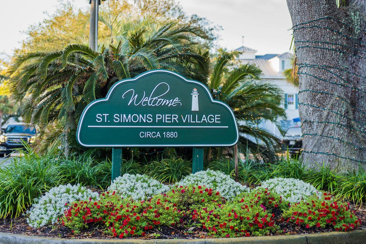 Welcome sign for St. Simons Pier Village with a lighthouse icon, surrounded by plants and greenery.