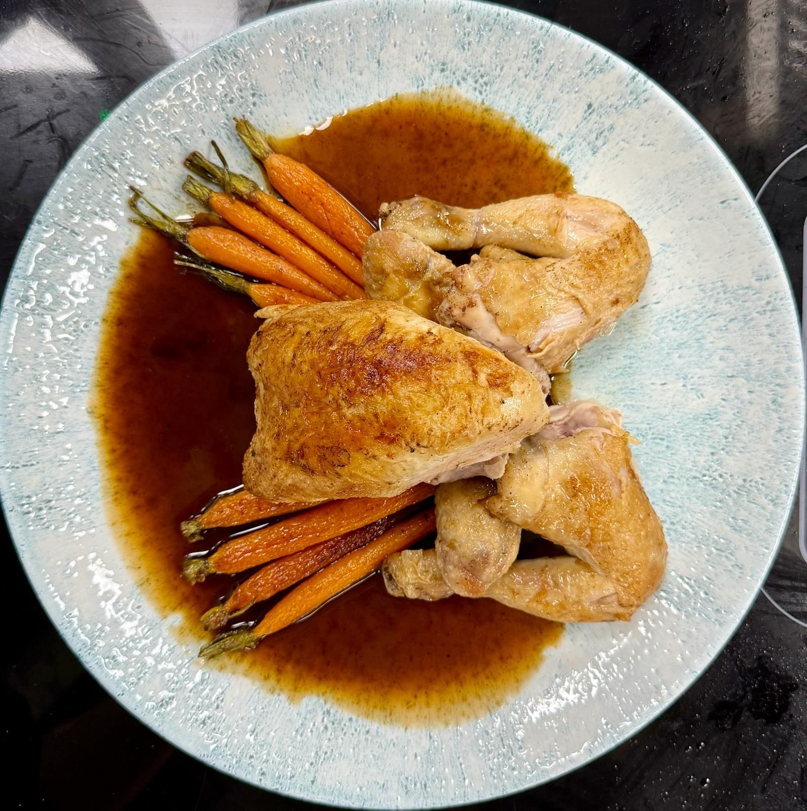 Roasted chicken pieces, carrots, and gravy on a blue-rimmed plate.