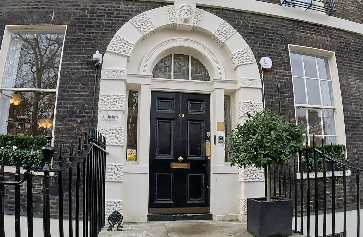 Black front door with arched white trim and a small potted tree, set in a brick building.