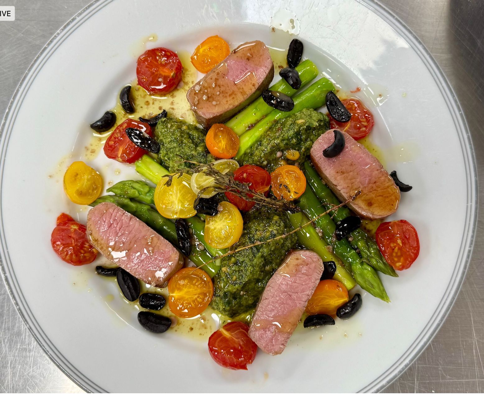 Plate of duck breast slices, asparagus, tomatoes, olives, and pesto.