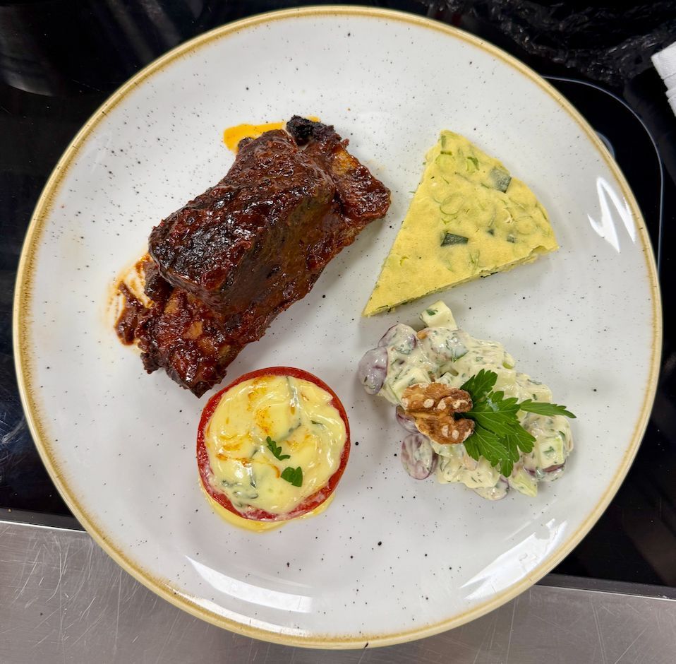 Plate with glazed meat rib, blue cheese wedge, potato salad, and tomato.