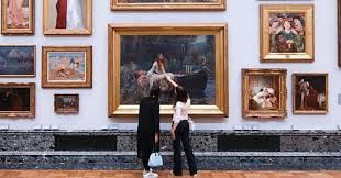 Two people looking at a painting in a museum, surrounded by other framed art.