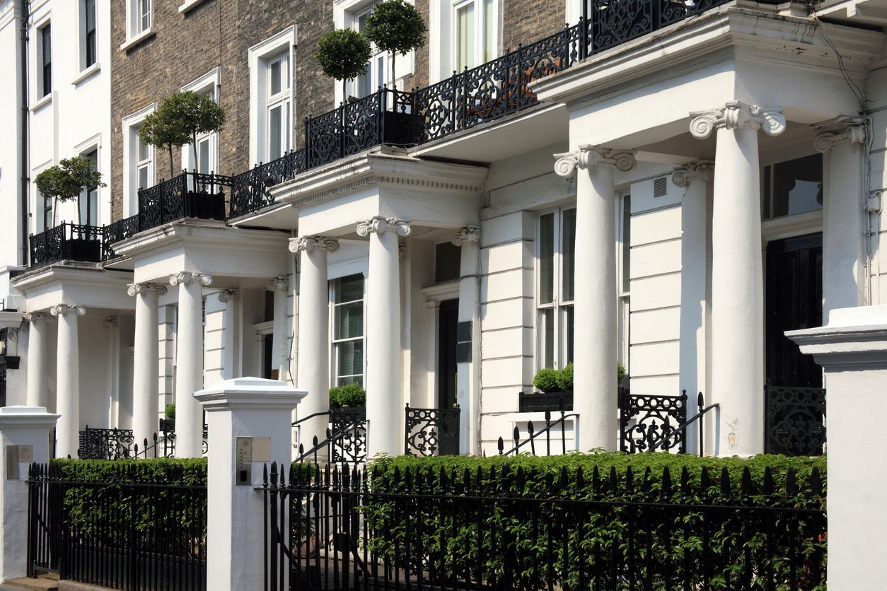 Row of elegant white townhouses with black wrought iron balconies and green hedges.