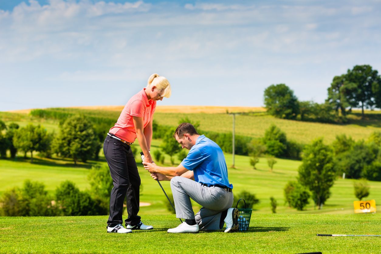 Golf instructor helping a woman with her swing on a sunny green golf course.