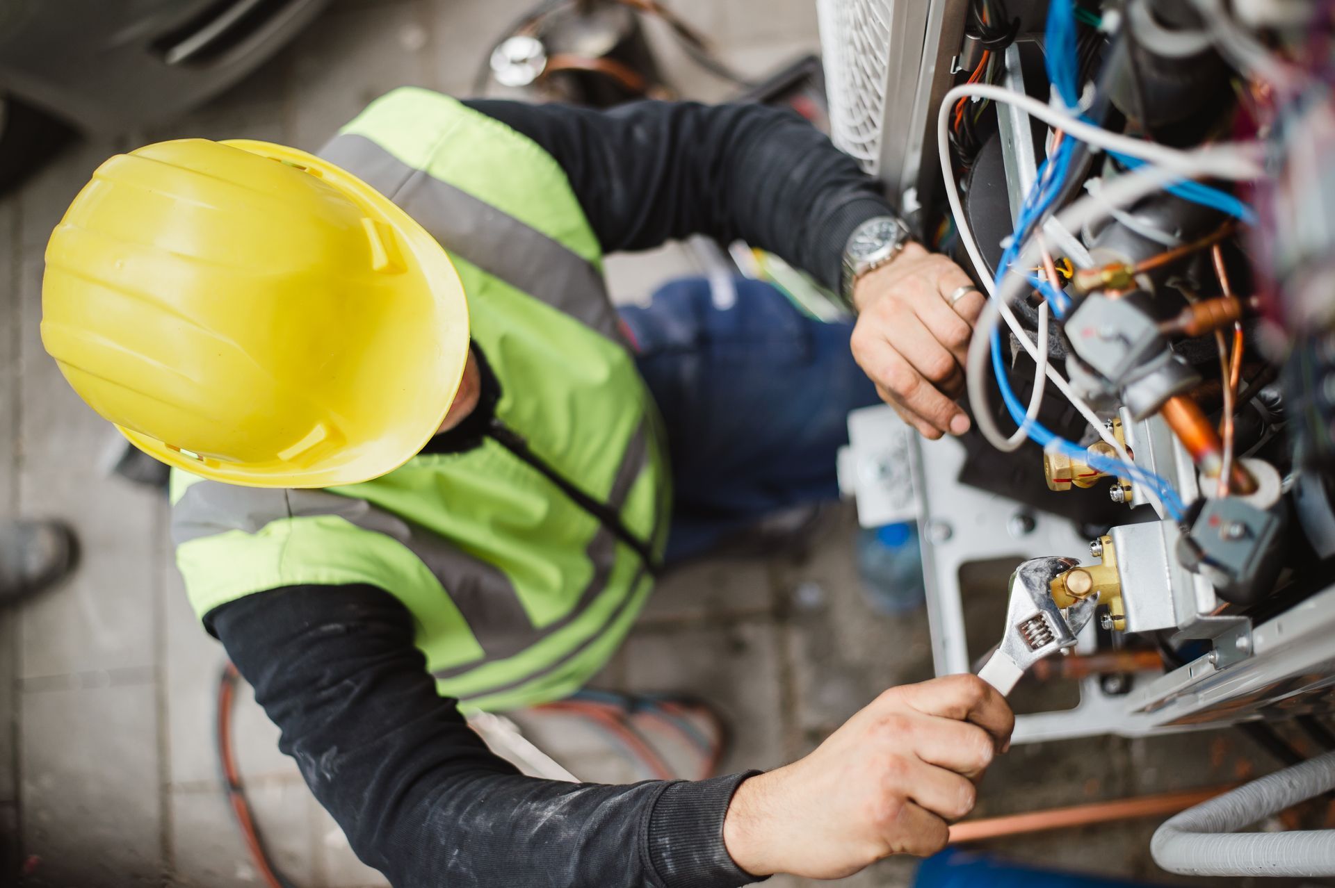 A man wearing a hard hat and safety vest is working on a machine.