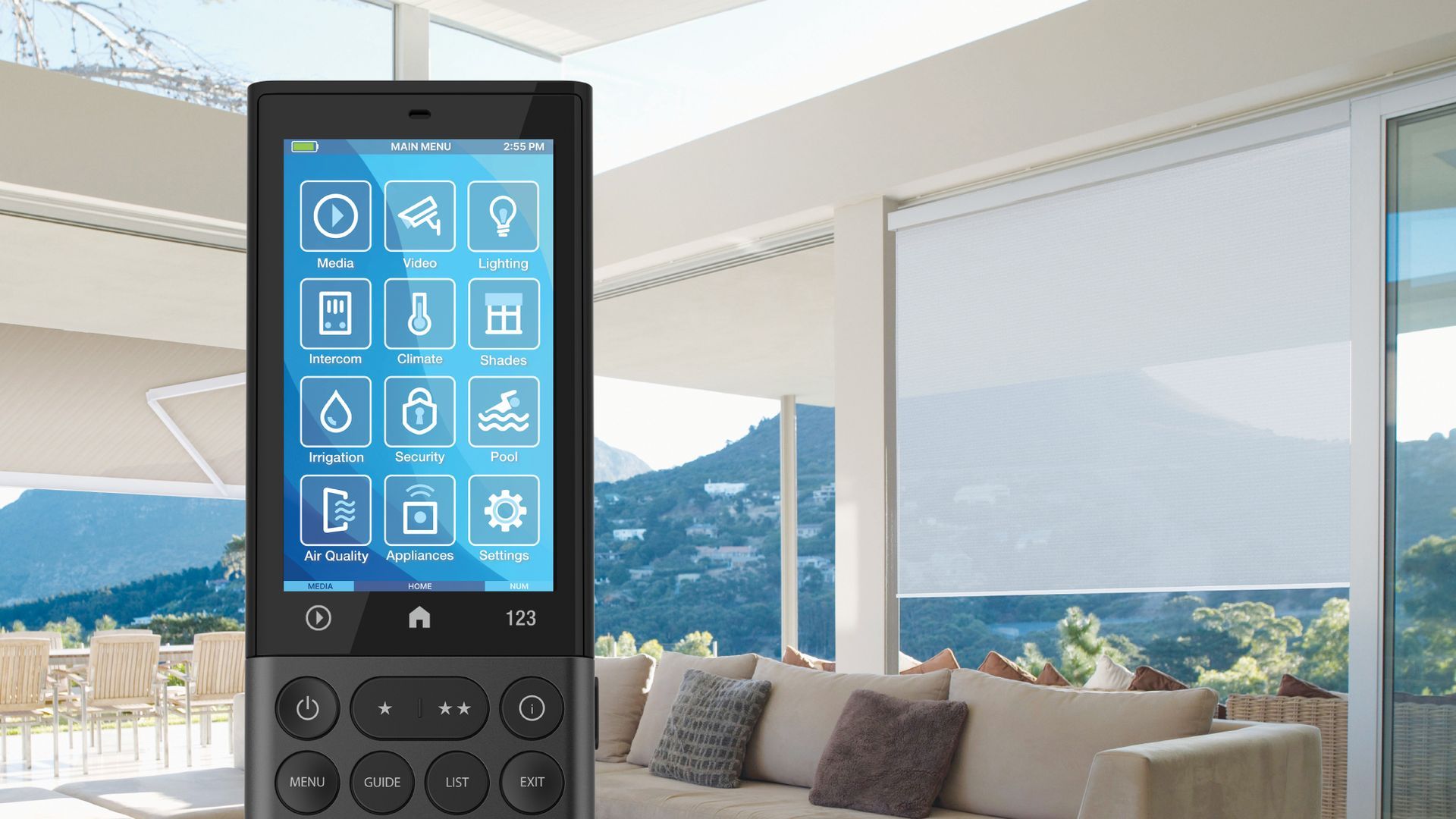 Smart home remote with blue touchscreen icons in a bright living room overlooking mountains and sea