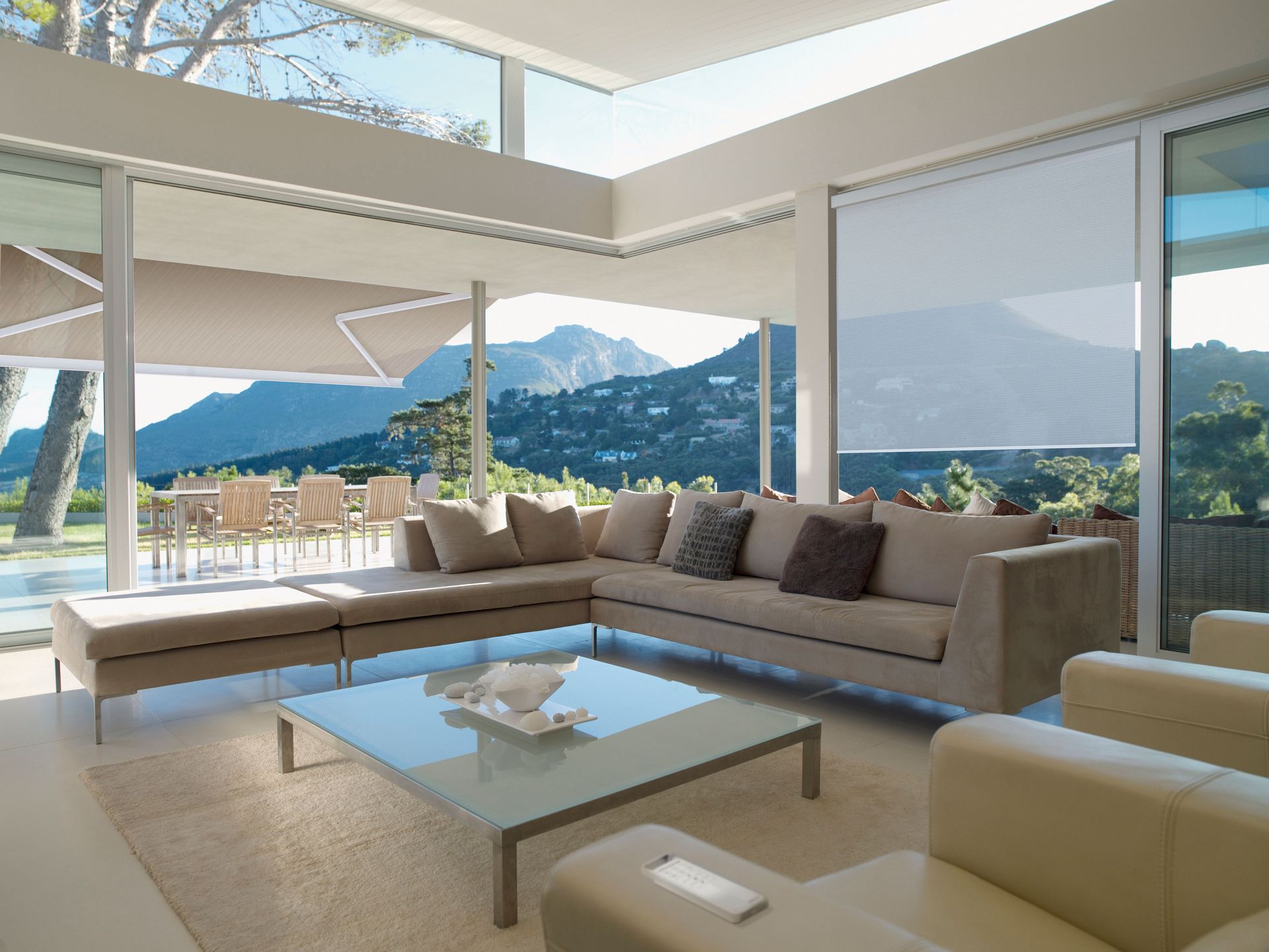 Modern living room with beige sectional, glass coffee table, and mountain view through large windows