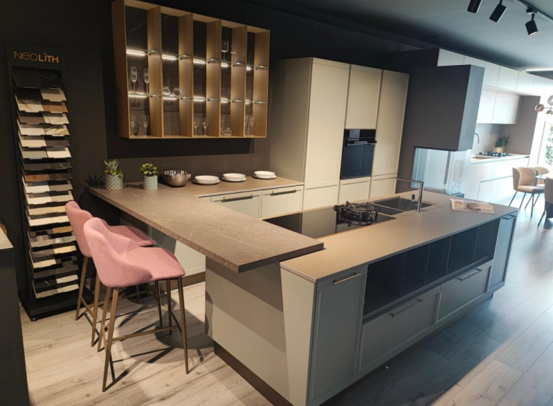 Esposizione di una cucina moderna: mobili beige, isola con piano cottura, piano di lavoro marrone, sgabelli da bar rosa.