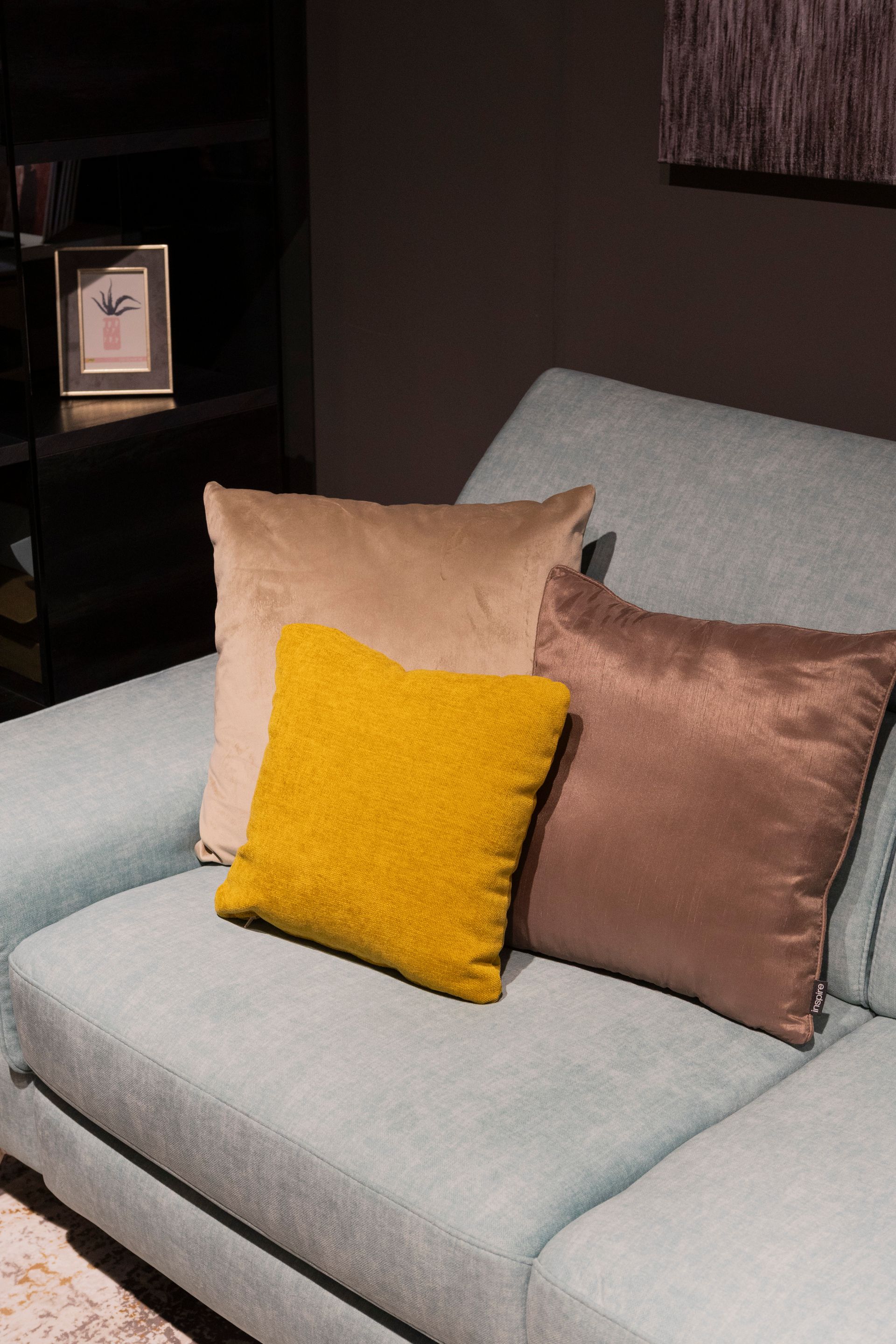 Tre cuscini su un divano turchese: senape, beige e marrone. Parete scura sullo sfondo.