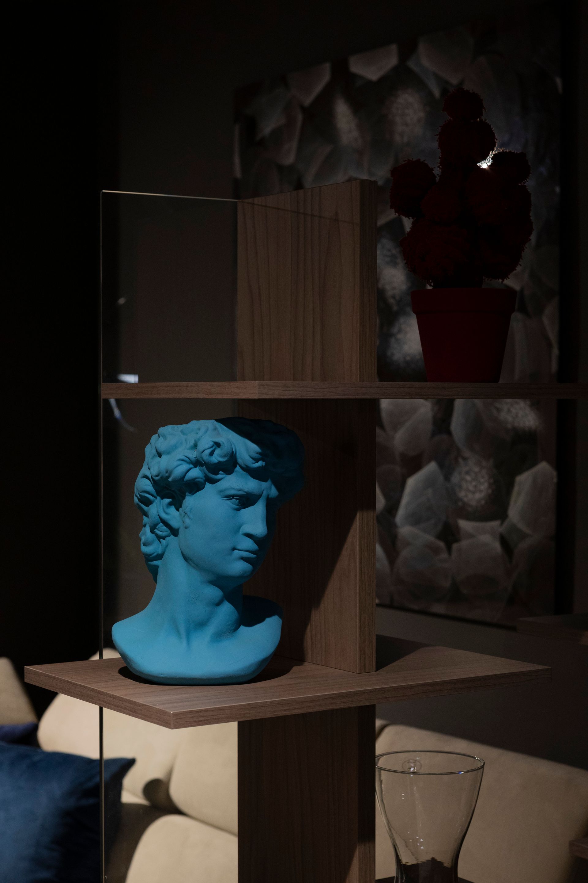 Scultura a forma di busto blu su mensola con cactus rosso e parete strutturata sullo sfondo.