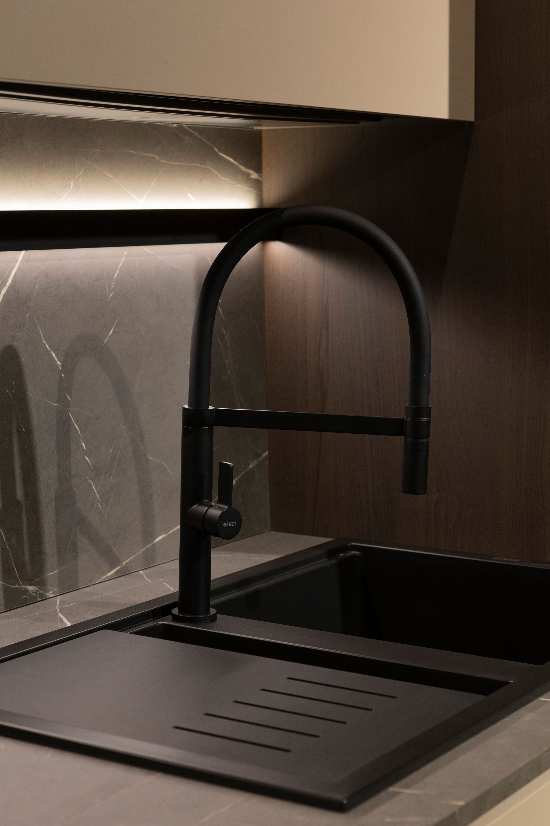 Rubinetto da cucina nero sopra un lavello nero con scolapiatti; piano di lavoro e paraschizzi grigio scuro; illuminazione sotto i pensili.