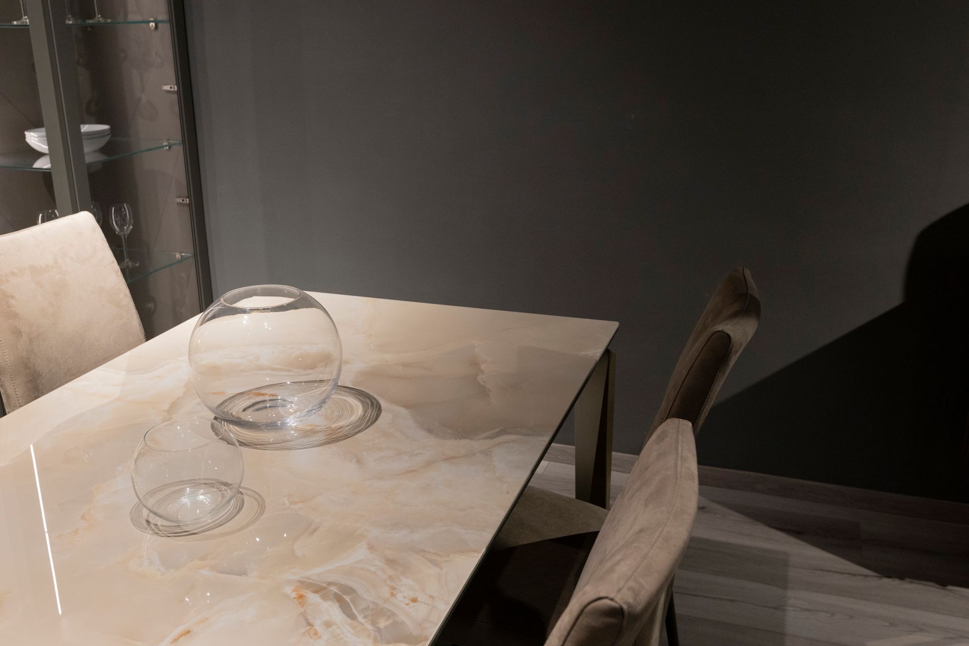 Tavolo da pranzo con ciotola di vetro su una superficie marmorizzata, due sedie e una parete scura.