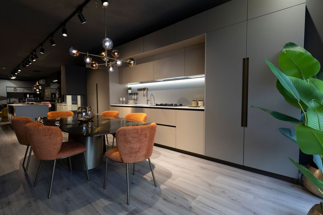 Cucina moderna con zona pranzo. Mobili grigi, sedie arancioni, tavolo nero e pianta rigogliosa.