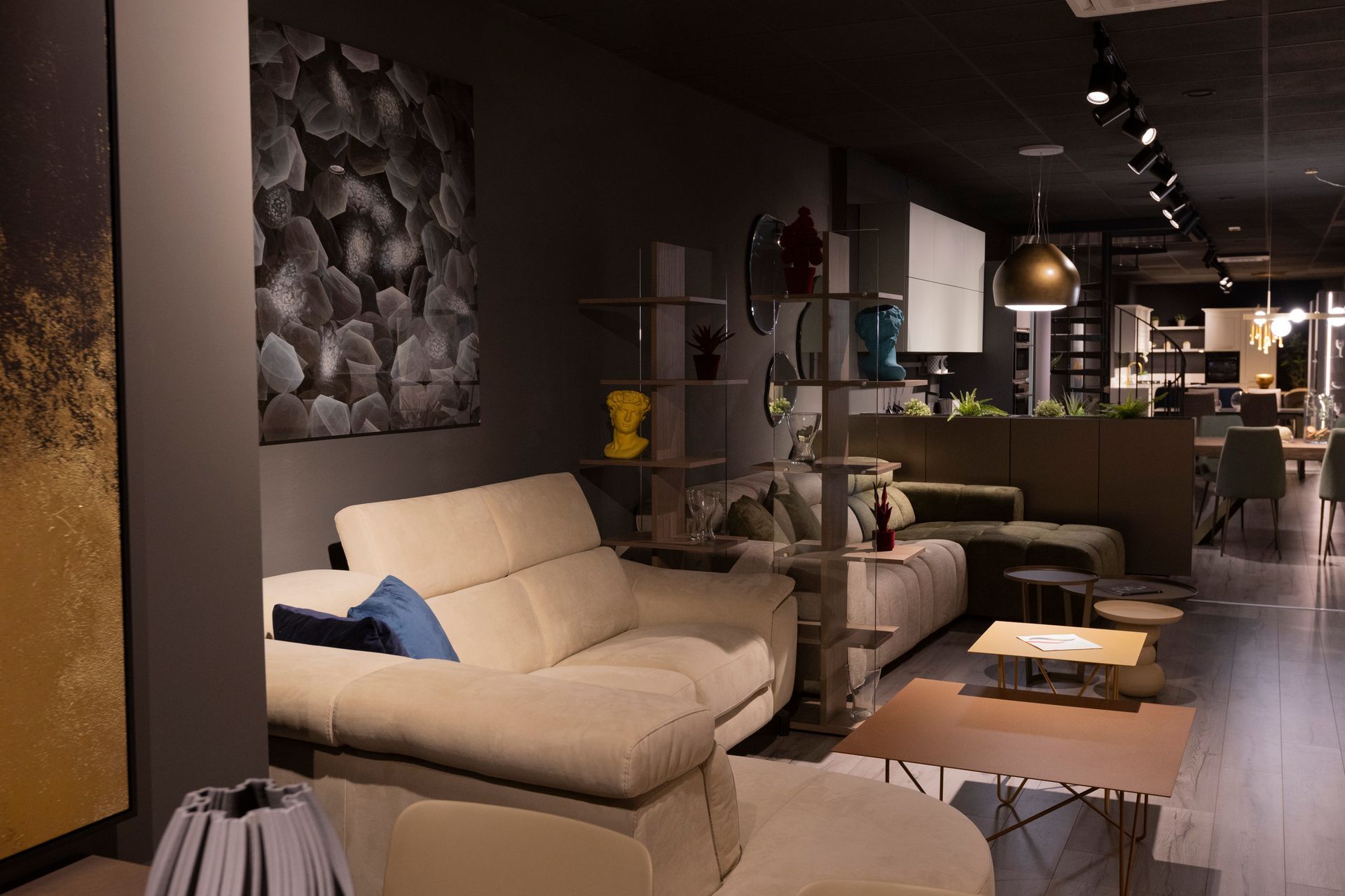 Esposizione di mobili per il soggiorno. Divano componibile beige, arte astratta, pareti scure, mensole con decorazioni.