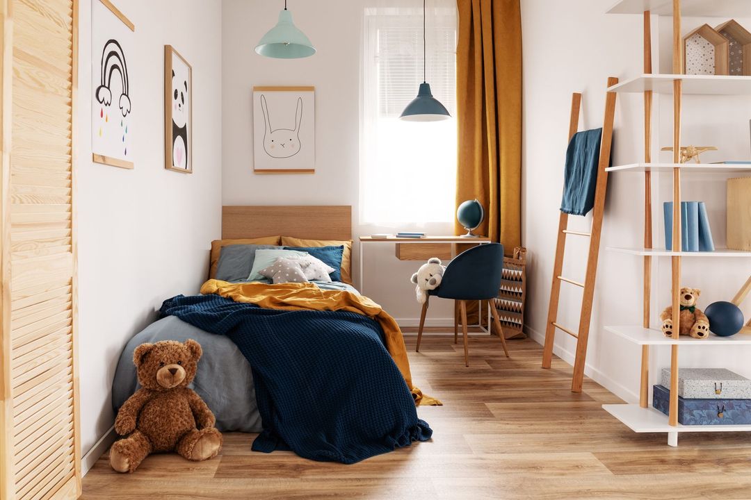 Accogliente camera da letto con letto, scrivania e libreria. Biancheria da letto blu navy e senape, pavimenti in legno e dettagli azzurri.