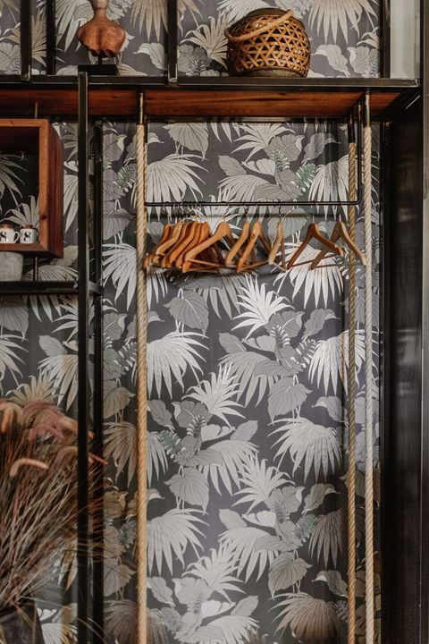 Scaffale con grucce in legno su sfondo di carta da parati floreale grigia e bianca.