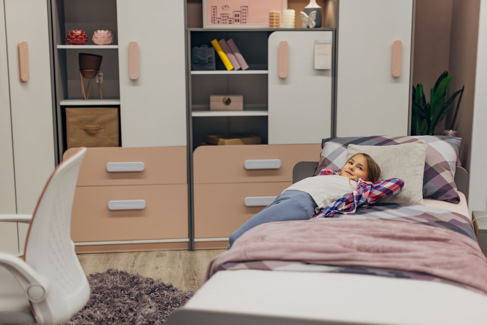 Un bambino è sdraiato su un letto in una camera da letto rosa e bianca e sorride alla telecamera.