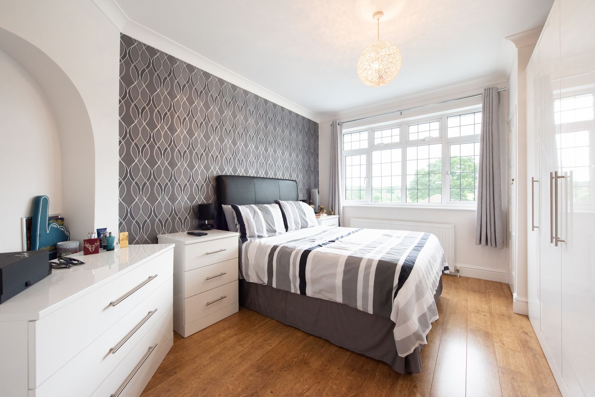 Camera da letto con letto, mobili bianchi, parete strutturata e finestra.