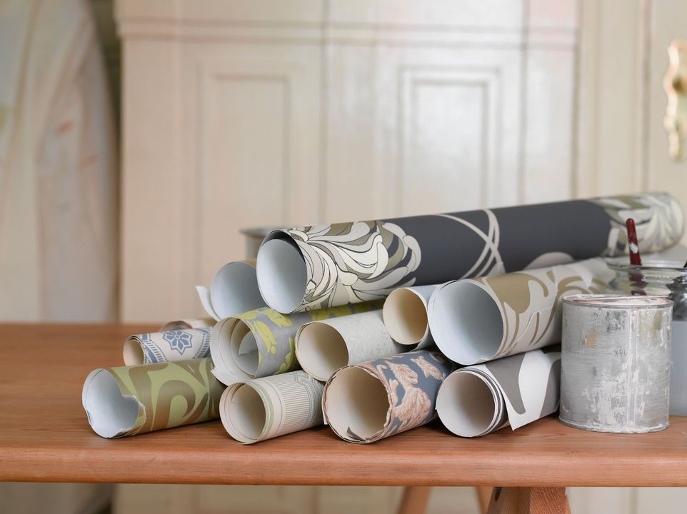 Campioni di carta da parati arrotolata impilati su un tavolo di legno, su uno sfondo di colore chiaro.