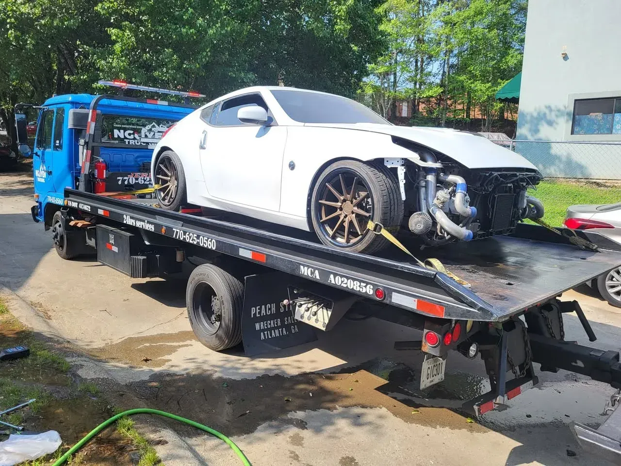 White car with front-end damage on a flatbed tow truck.