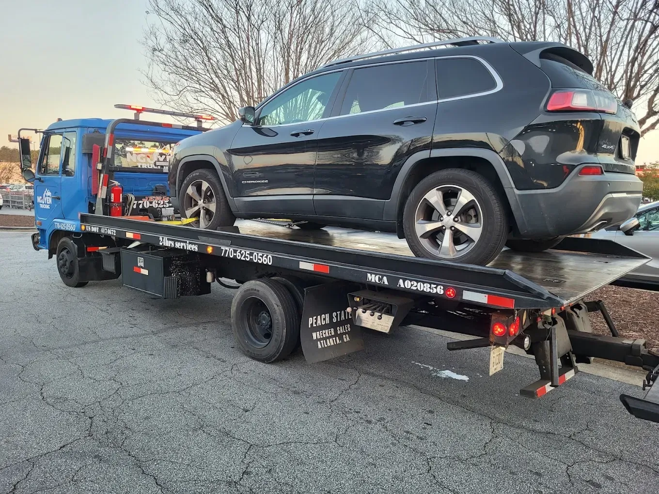 Black SUV loaded on a blue tow truck, parked on asphalt.