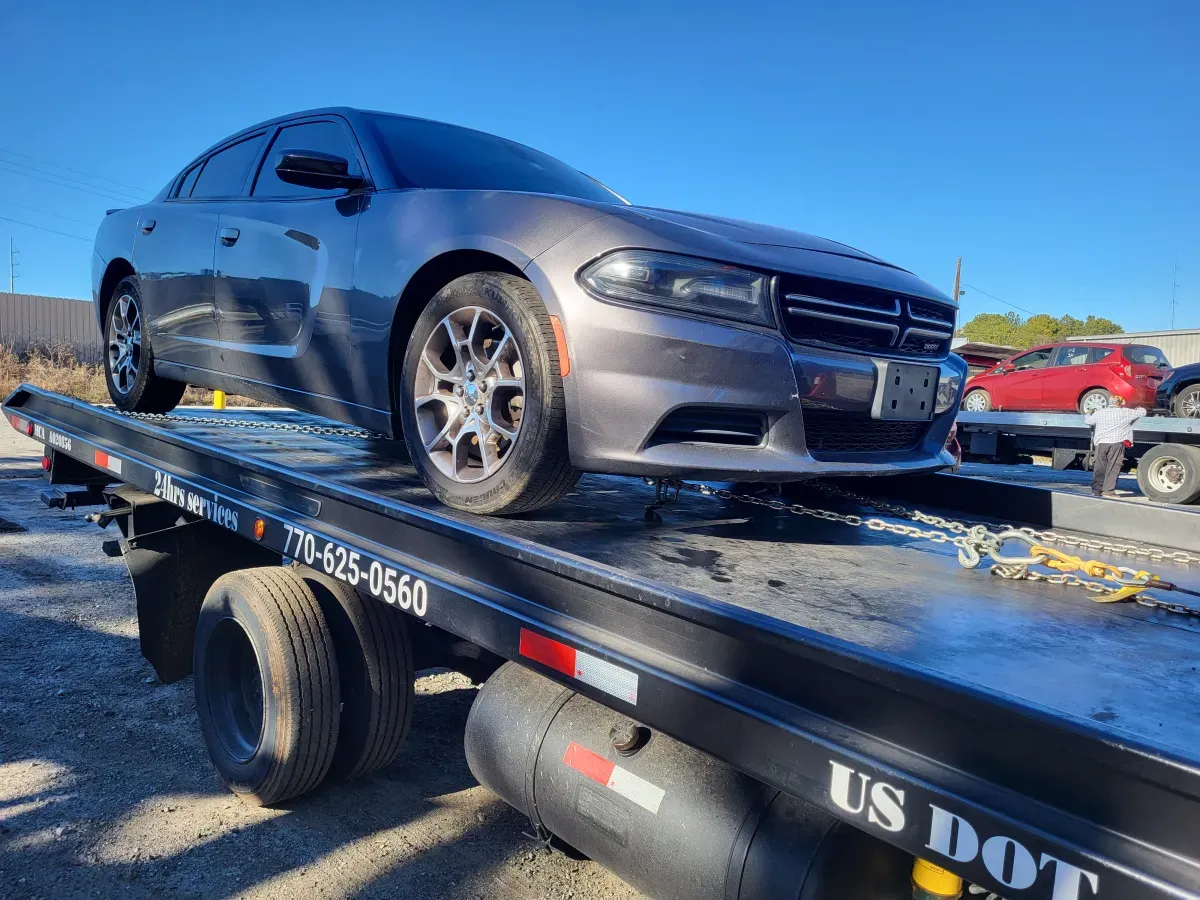Gray Dodge Charger on a tow truck, outdoors in a sunny setting.