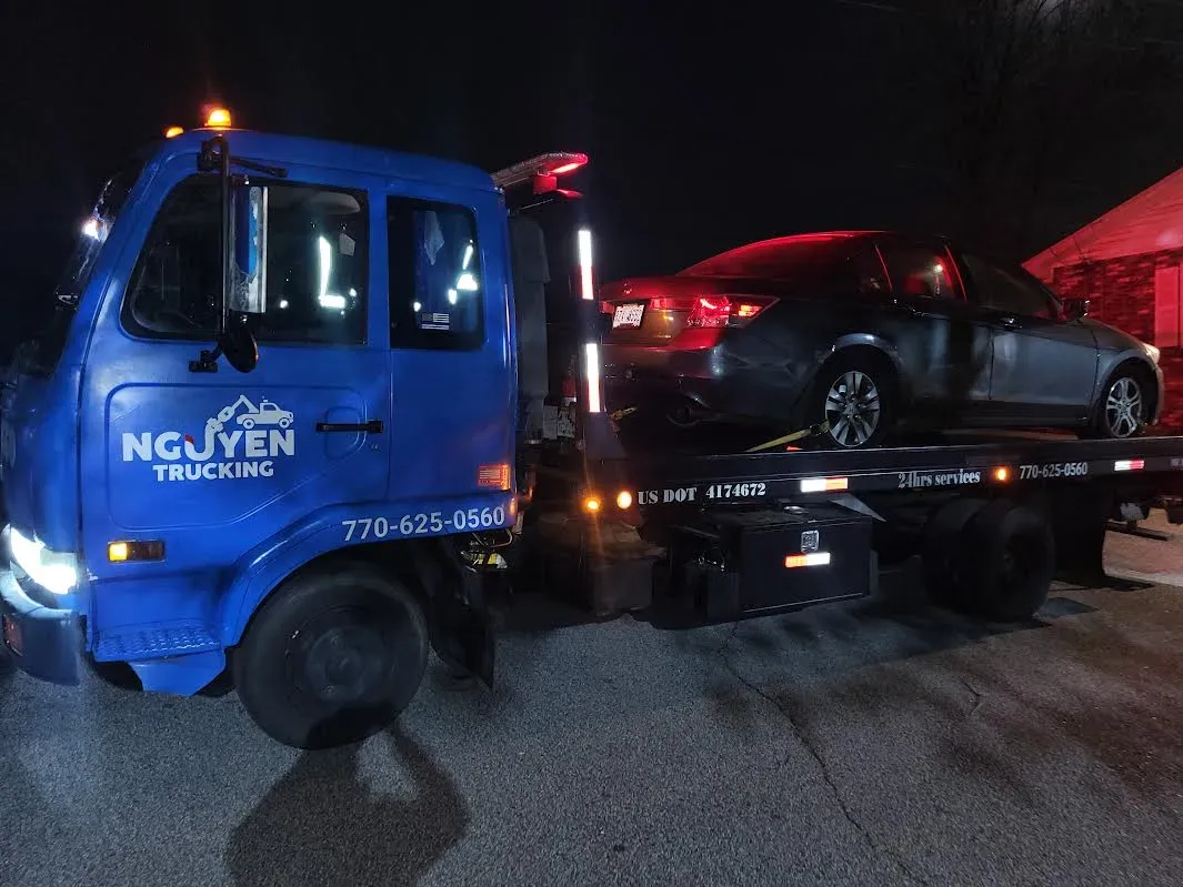 Blue tow truck with a car on the flatbed at night. 