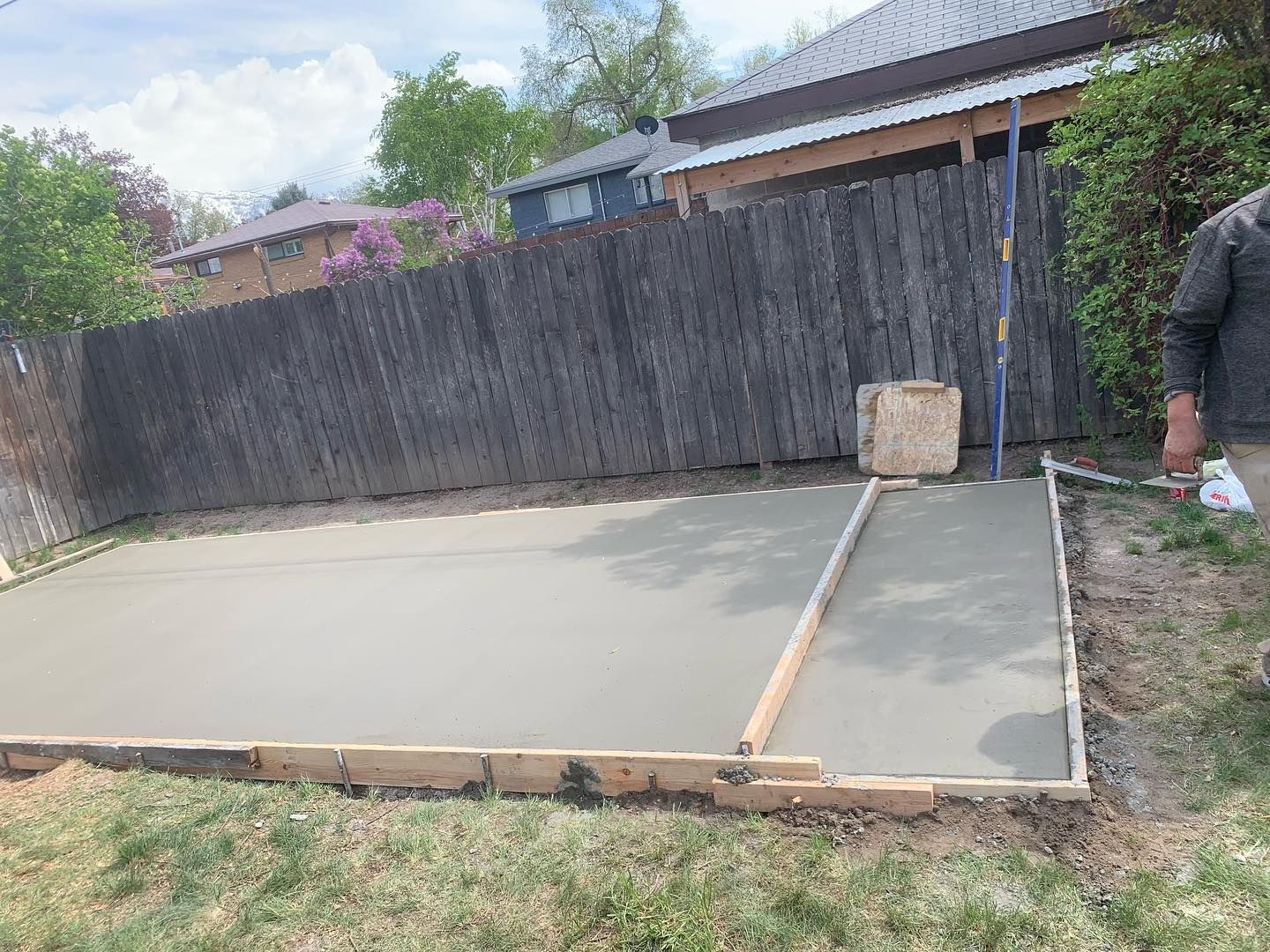 A man is working on a concrete slab in a backyard.