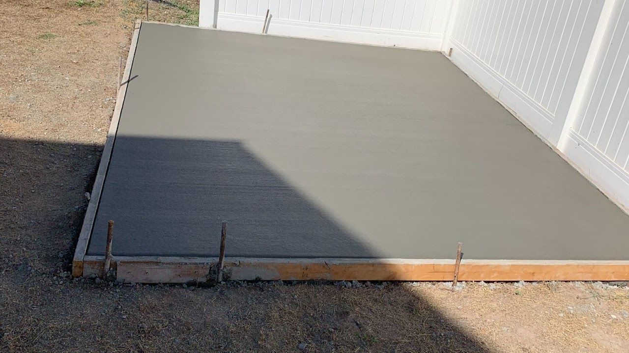 A concrete floor is being built in front of a white fence.
