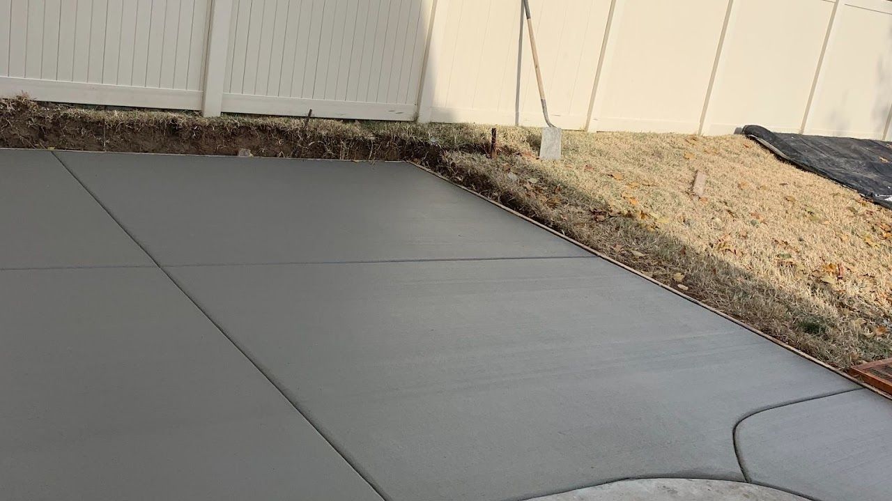 A concrete patio with a white fence in the background.