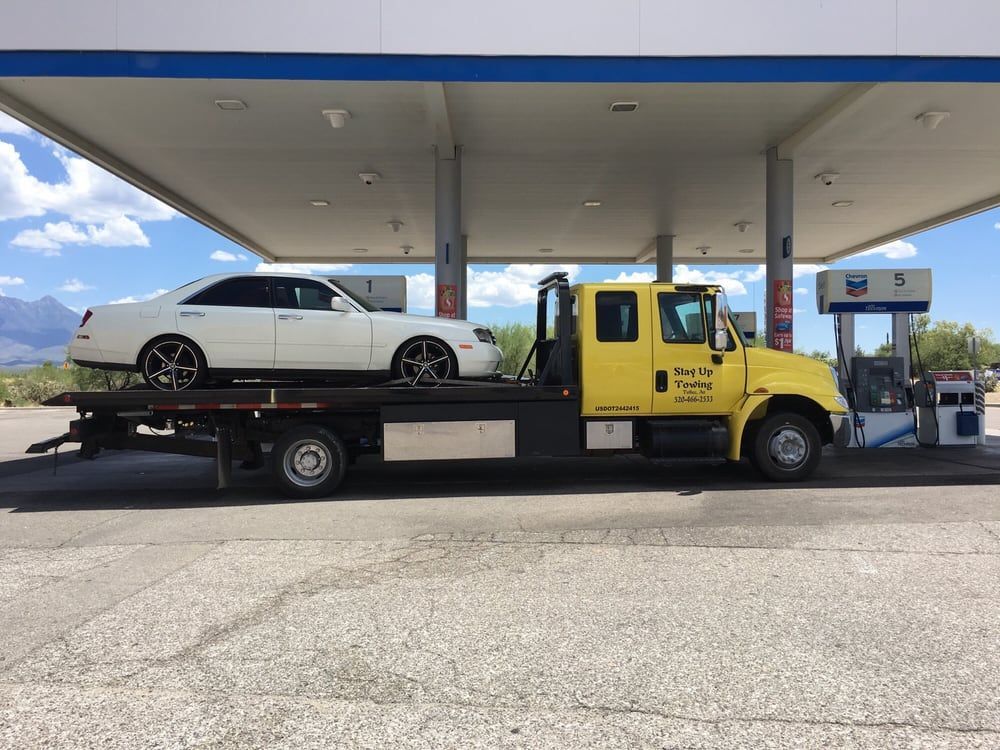 A yellow tow truck with a white car on the back is parked at a gas station. A yellow tow truck with a white car on the back is parked at a gas station.