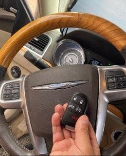A person is holding a car key in front of a steering wheel. A person is holding a car key in front of a steering wheel.