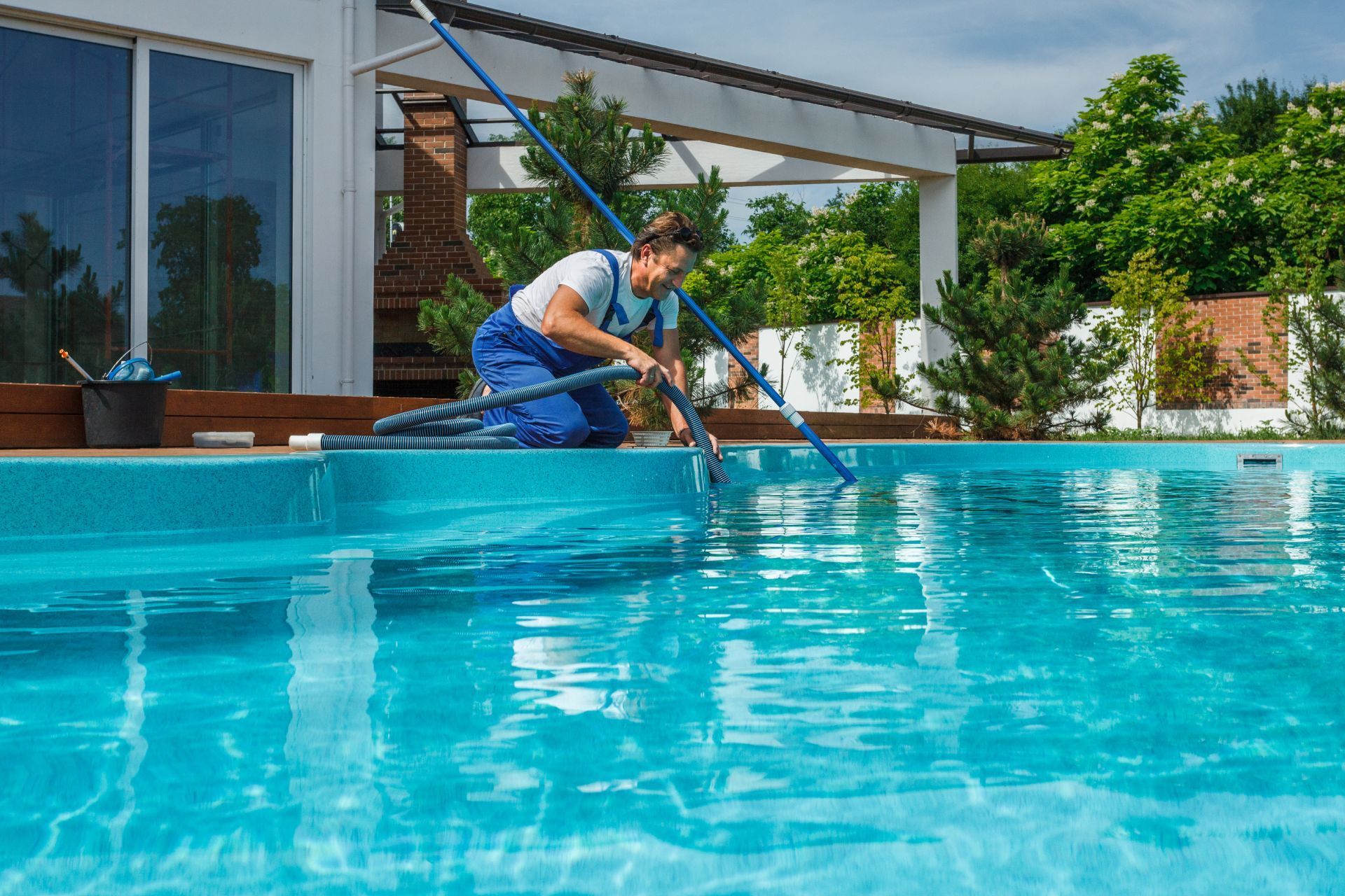 A man is cleaning a swimming pool with a vacuum cleaner.
