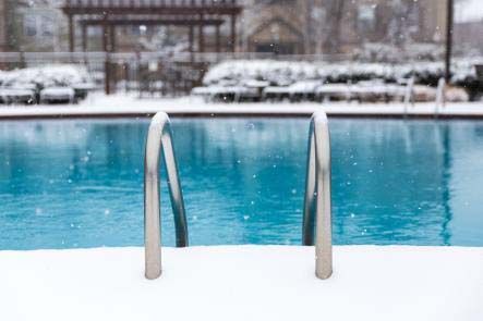 Snowy scene with a blue swimming pool and silver ladder. White snow surrounds the pool's edge.