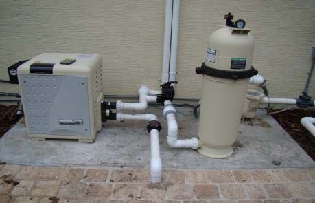 Pool equipment, including a pump and filter, on a concrete pad. White and beige components with plumbing.