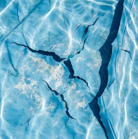 Cracked blue surface under water with sun reflections and dark shadows.