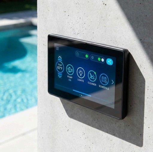 Black touchscreen control panel on concrete wall by a pool. Display shows various pool system controls.