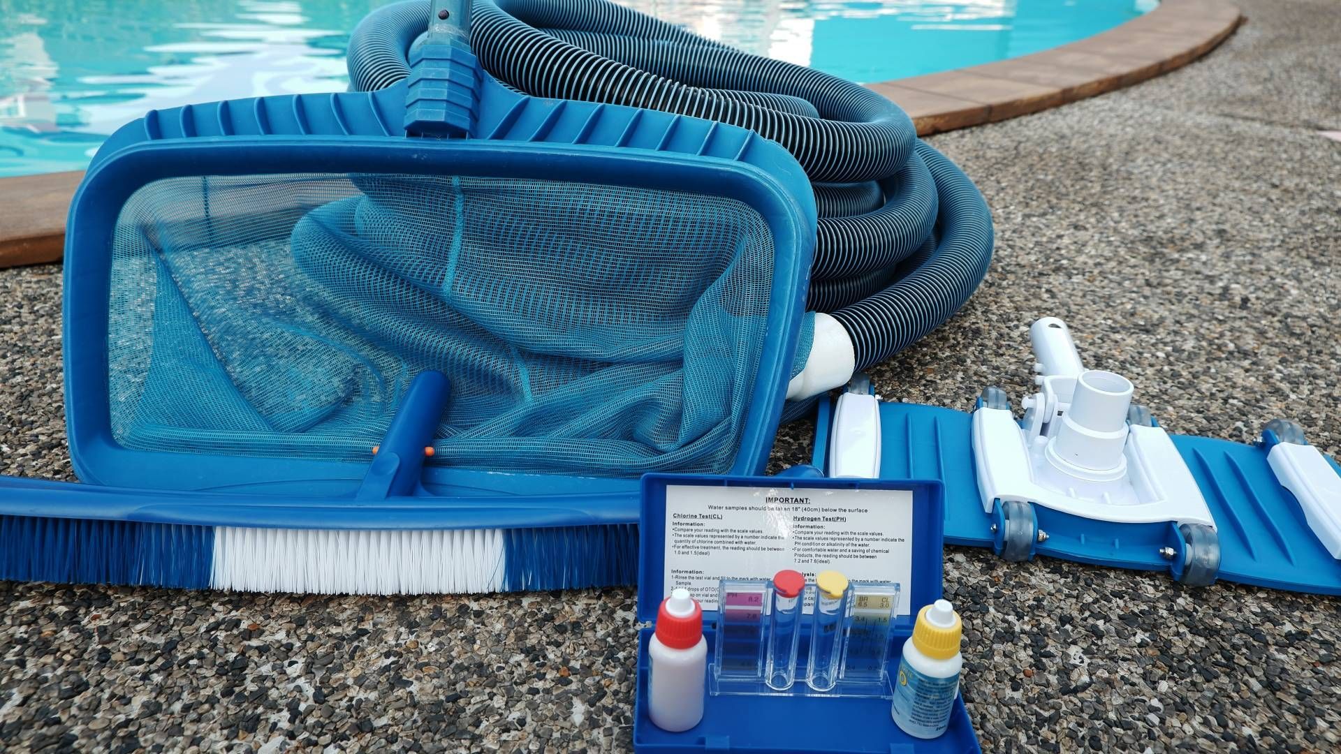 Pool cleaning supplies including a net, brush, hose, vacuum, and water test kit, sitting by a pool.