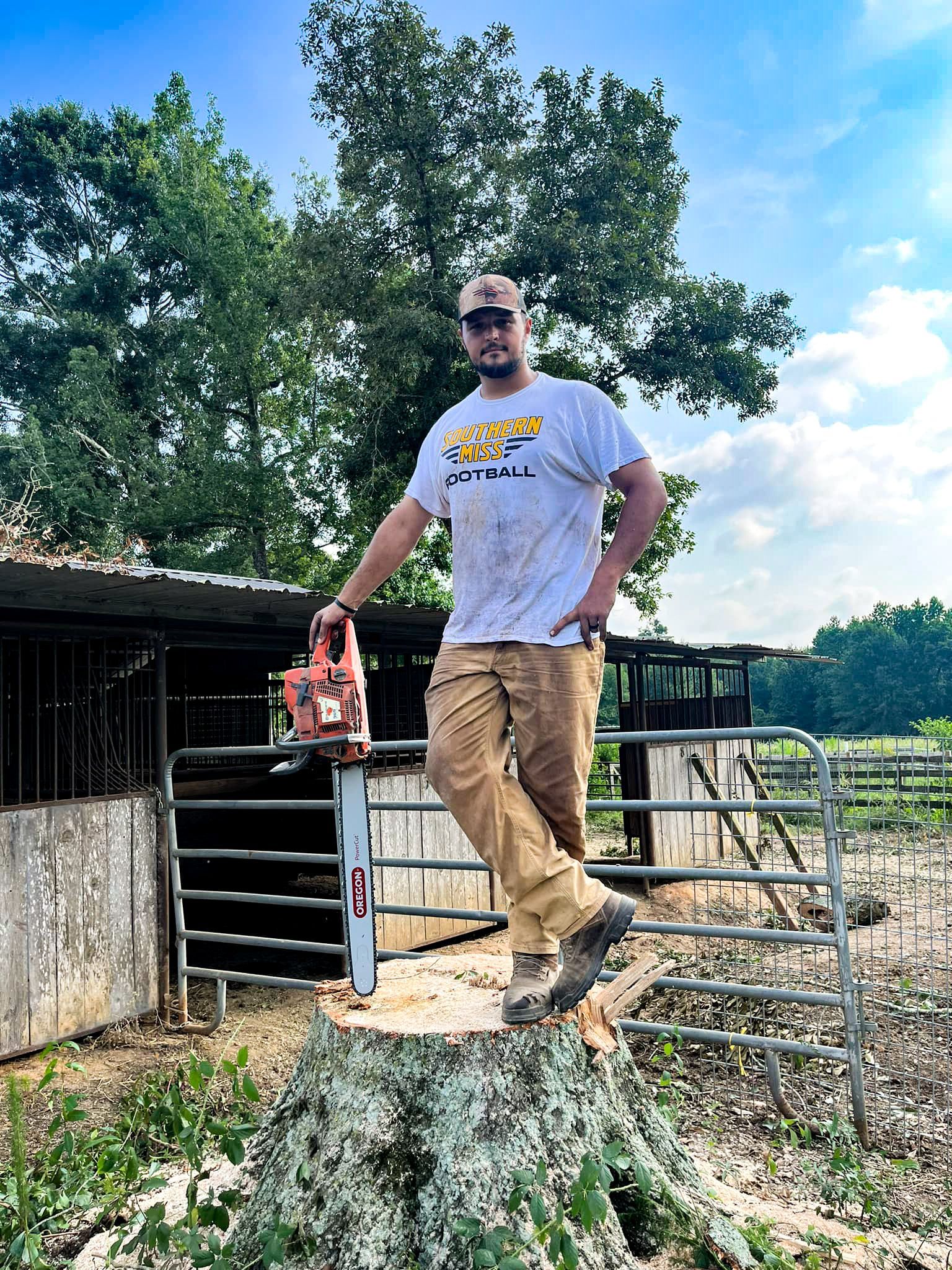 A man is standing on top of a tree stump holding a chainsaw.