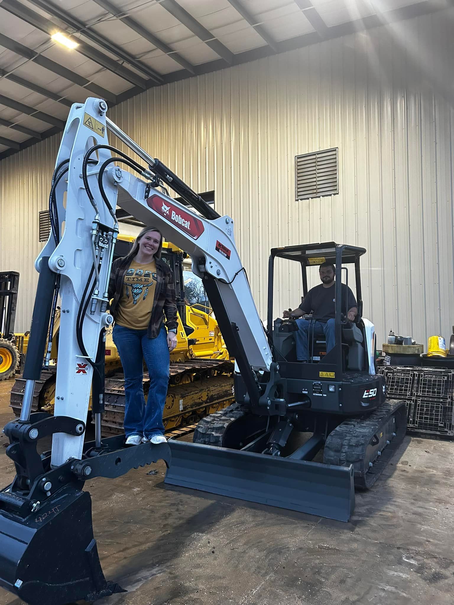 A man is standing next to a bulldozer in a warehouse.