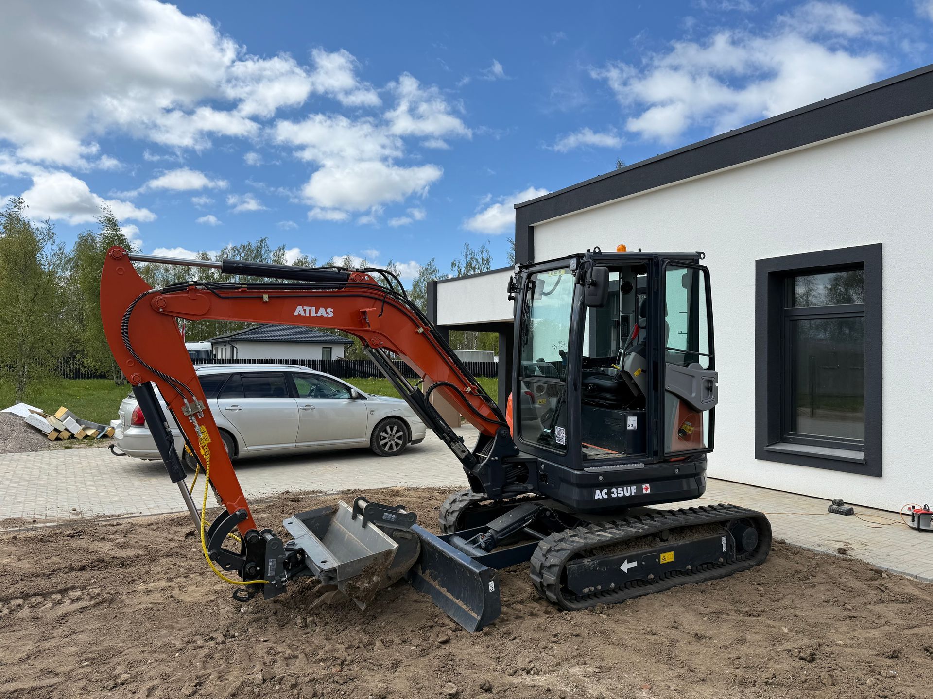 Prie balto namo stovi nedidelis ekskavatorius.