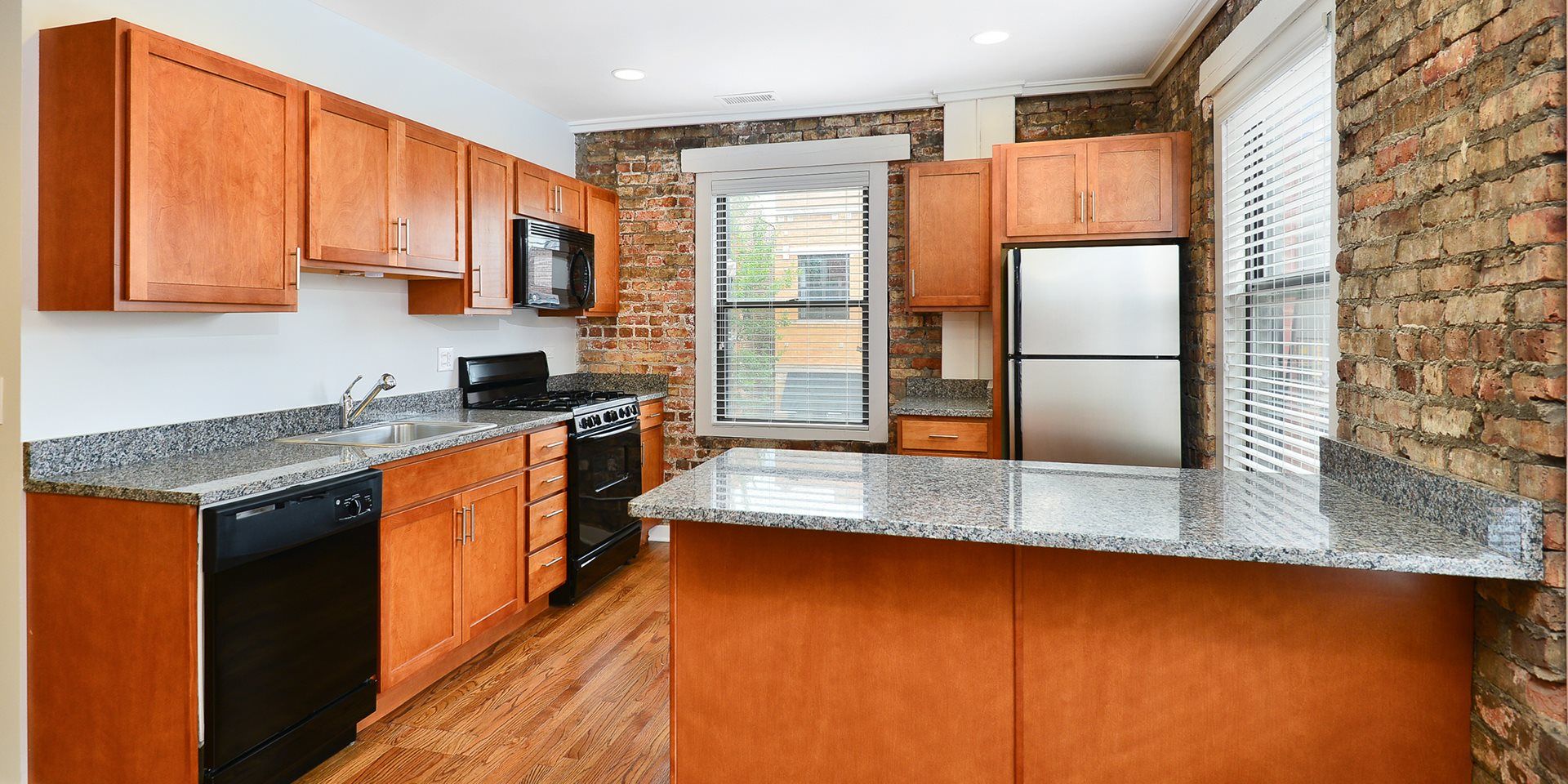 A kitchen with wooden cabinets , granite counter tops , stainless steel appliances and a large island at 1640 N Damen Apartments.