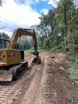 Yellow excavator clearing a muddy path through a forest.
