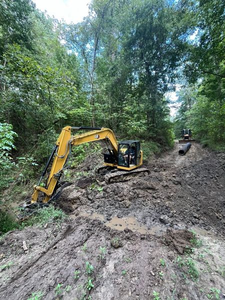 Yellow excavator working in muddy area beside trees.