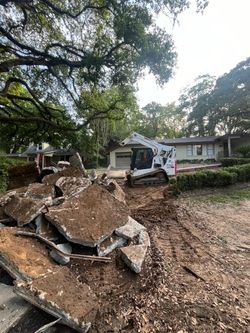Bobcat removing concrete rubble from driveway in front of a mid-century modern house.