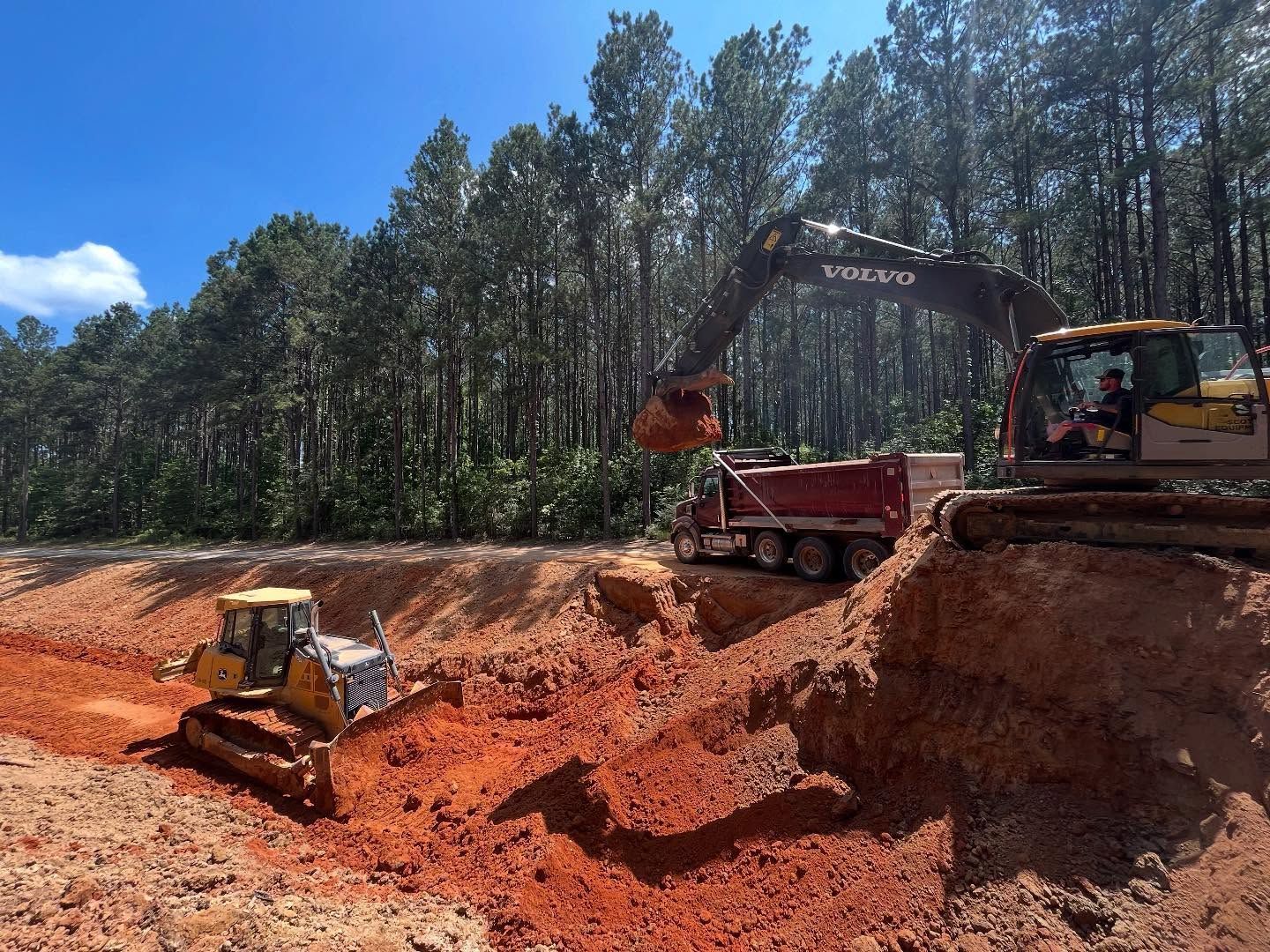 Construction site with excavator, bulldozer, and dump truck removing dirt.