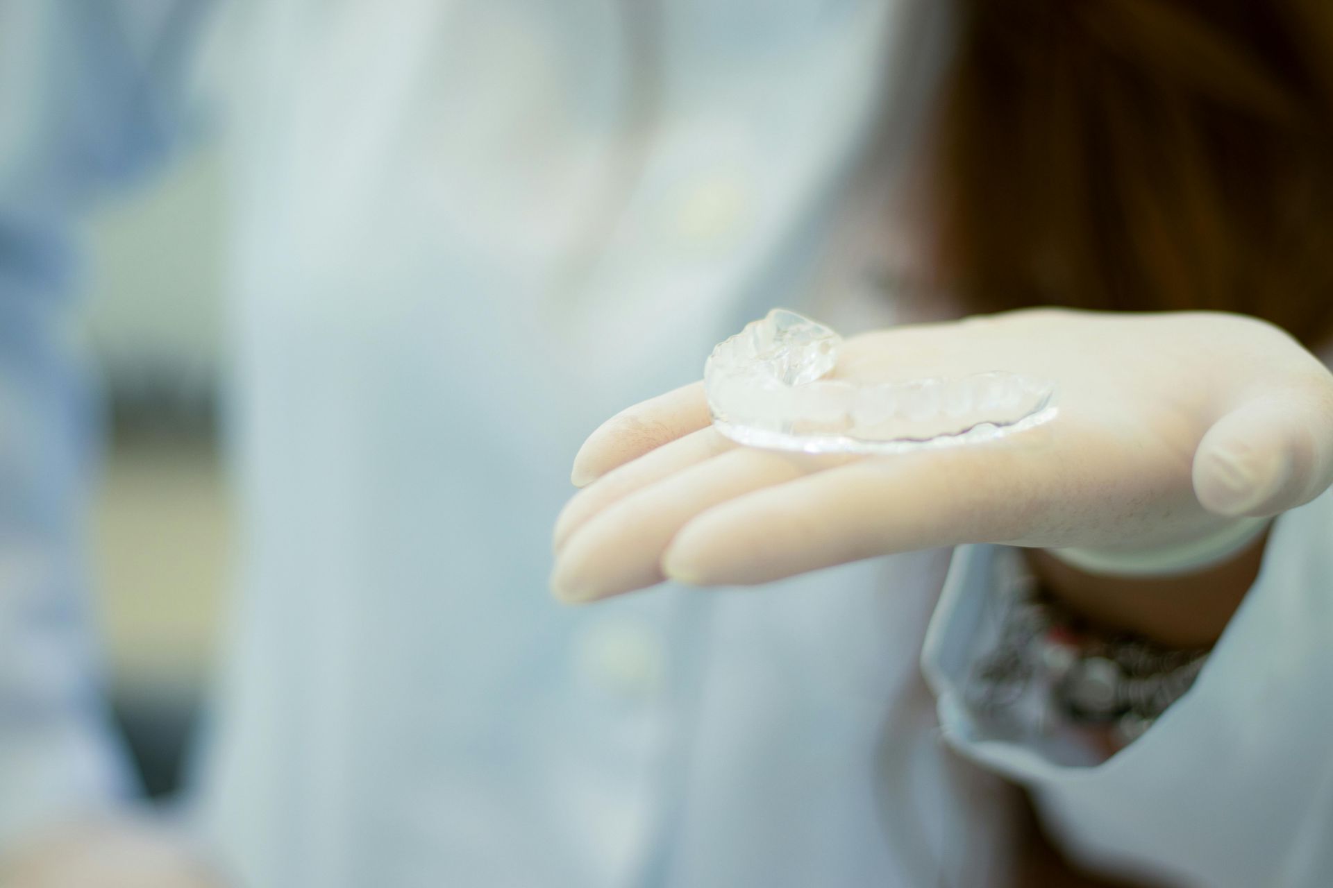 A gloved hand holding a clear dental retainer.