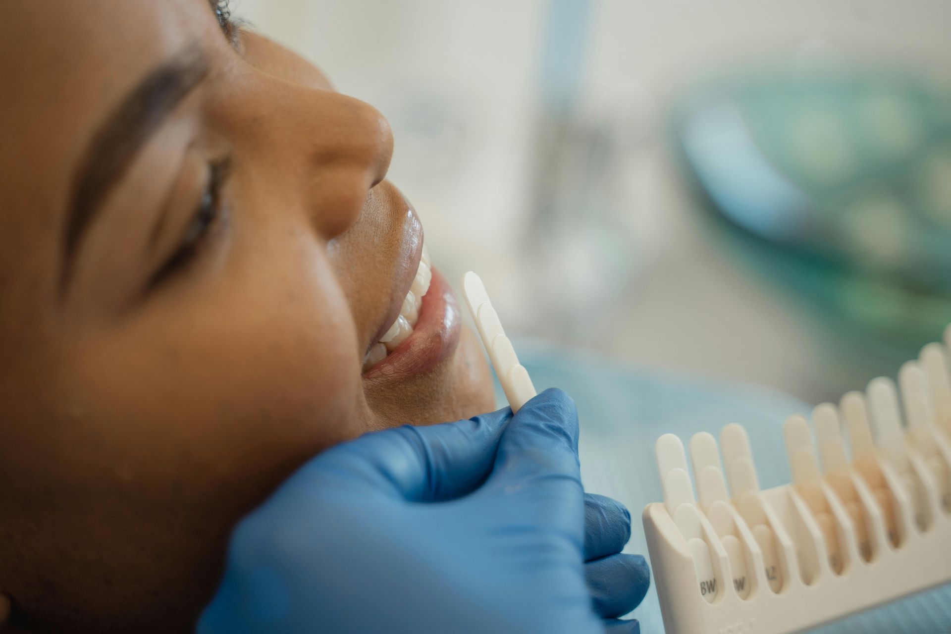 Dentist examining a patient's teeth with shade guide in a dental clinic.