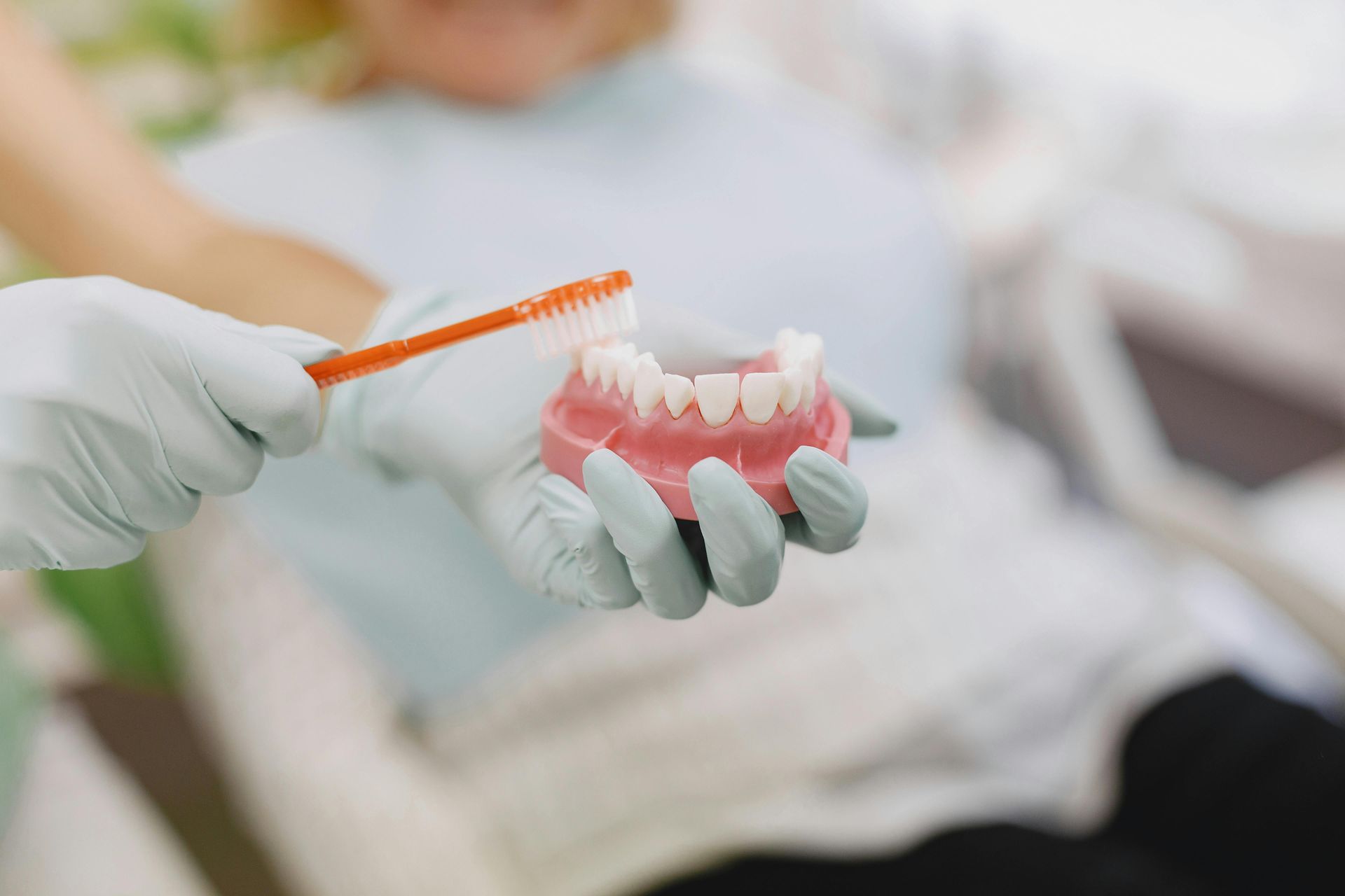 Gloved hand brushing a set of dentures. Patient in dental chair.